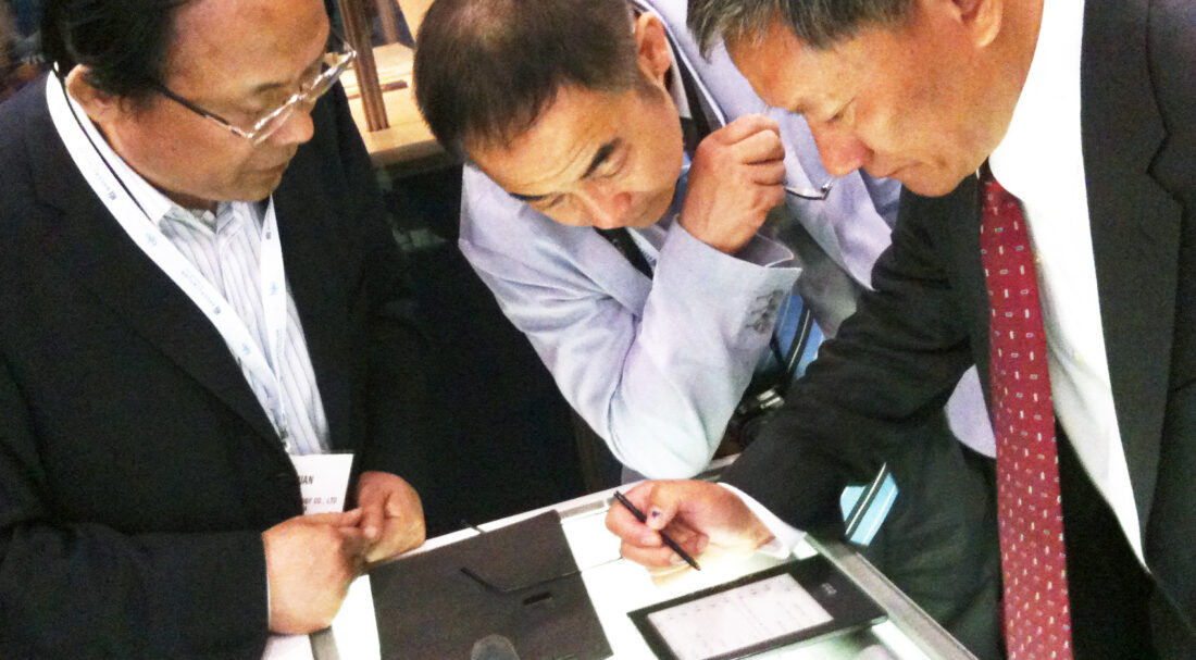 Three people in suits looking at an ebook reading device